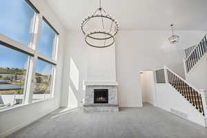 Unfurnished living room featuring carpet flooring, a stone fireplace, a towering ceiling, and a chandelier