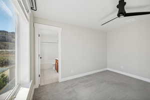 Unfurnished bedroom with connected bathroom, light colored carpet, and ceiling fan