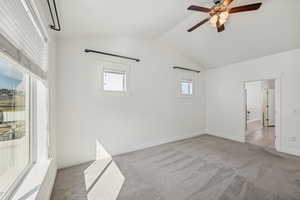 Empty room with vaulted ceiling, light carpet, and ceiling fan