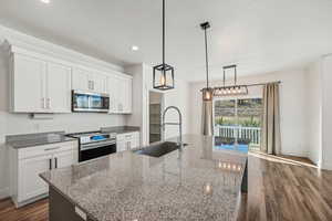 Kitchen featuring sink, appliances with stainless steel finishes, white cabinetry, and an island with sink