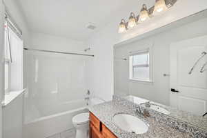 Full bathroom with vanity, toilet, tile patterned floors, and washtub / shower combination