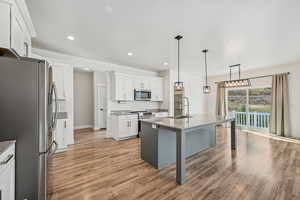 Kitchen with sink, stainless steel appliances, white cabinets, light hardwood / wood-style flooring, and a center island with sink