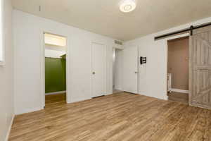 Unfurnished bedroom with a textured ceiling, a barn door, ensuite bathroom, light hardwood / wood-style floors, and a closet