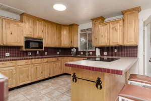 Kitchen featuring tile countertops, black appliances, and decorative backsplash