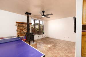 Game room featuring light tile patterned floors, a textured ceiling, a wood stove, and ceiling fan