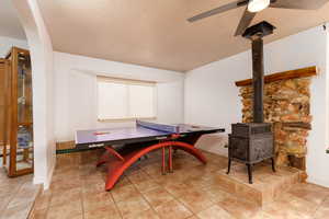 Rec room with ceiling fan, a wood stove, a textured ceiling, and light tile patterned floors