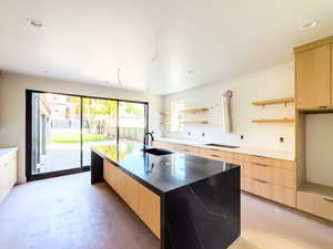 Kitchen with light brown cabinetry, sink, light wood-type flooring, and a kitchen island with sink