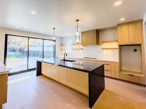 Kitchen with light brown cabinets, light hardwood / wood-style floors, sink, and decorative light fixtures