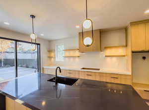 Kitchen featuring pendant lighting, light brown cabinets, sink, and cooktop