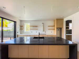 Kitchen featuring dark stone countertops, light brown cabinetry, sink, and a kitchen island with sink