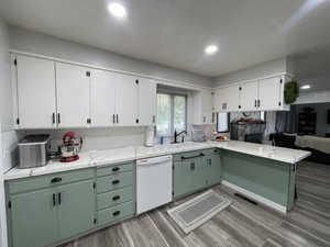 Kitchen featuring wood-type flooring, sink, green cabinetry, white dishwasher, and kitchen peninsula