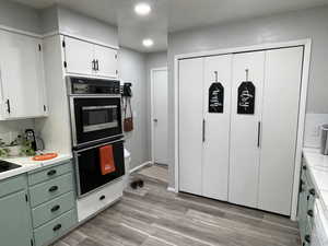 Kitchen featuring green cabinetry, light wood-type flooring, black double oven, and white cabinets