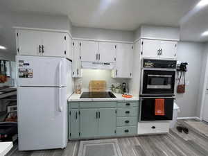 Kitchen featuring black appliances, green cabinets, white cabinets, decorative backsplash, and light hardwood / wood-style flooring