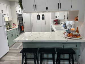 Kitchen with sink, kitchen peninsula, a kitchen breakfast bar, white cabinetry, and white fridge