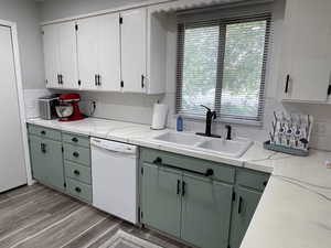 Kitchen featuring sink, light wood-type flooring, white dishwasher, green cabinets, and white cabinets