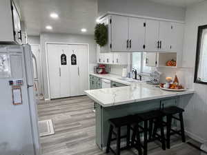 Kitchen featuring kitchen peninsula, white cabinets, a kitchen breakfast bar, sink, and white appliances