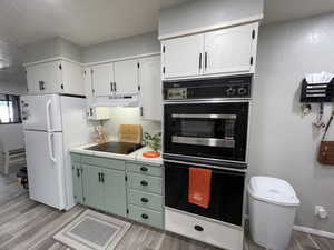 Kitchen with light hardwood / wood-style flooring, white cabinetry, black appliances, and green cabinetry