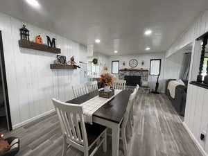 Dining room with a stone fireplace, wood walls, a textured ceiling, and wood-type flooring