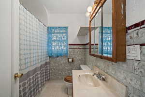 Bathroom featuring walk in shower, sink, tile walls, tile patterned flooring, and toilet