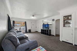 Carpeted living room featuring ceiling fan and a textured ceiling