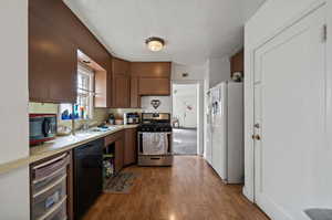 Kitchen with sink, light hardwood / wood-style floors, black appliances, and a textured ceiling