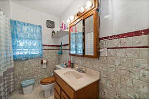 Bathroom featuring toilet, vanity, tile walls, and tile patterned flooring