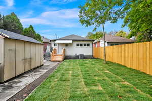 Back of house with a storage shed, a yard, and central AC unit