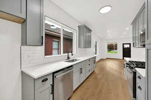 Kitchen featuring tasteful backsplash, appliances with stainless steel finishes, gray cabinetry, light hardwood / wood-style floors, and sink