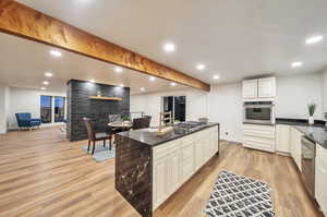 Kitchen featuring white cabinetry, a stone fireplace, stainless steel appliances, and light hardwood / wood-style floors