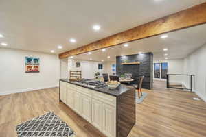 Kitchen with a stone fireplace, stainless steel gas cooktop, dark stone counters, a center island, and light hardwood / wood-style floors