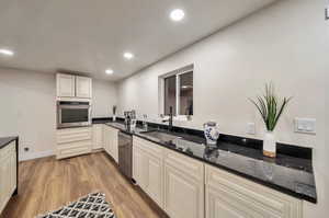 Kitchen with cream cabinets, dark stone countertops, sink, light wood-type flooring, and appliances with stainless steel finishes