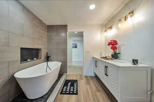 Bathroom featuring a tub, wood-type flooring, vanity, tile walls, and a textured ceiling