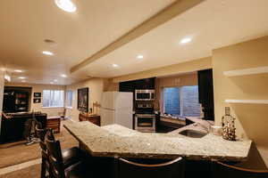 Kitchen featuring light stone countertops, appliances with stainless steel finishes, sink, kitchen peninsula, and light colored carpet