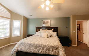 Carpeted bedroom featuring a textured ceiling, vaulted ceiling, and ceiling fan