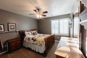 Bedroom with dark colored carpet, a textured ceiling, and ceiling fan