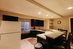 Kitchen with light stone countertops, sink, kitchen peninsula, a kitchen breakfast bar, and white refrigerator