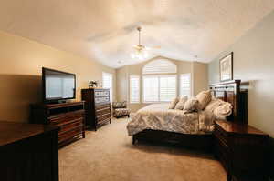 Bedroom with light carpet, a textured ceiling, vaulted ceiling, and ceiling fan