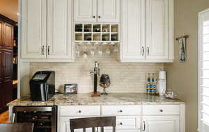 Bar with wine cooler, decorative backsplash, white cabinetry, and light stone countertops