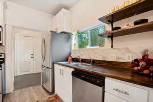 Kitchen with white cabinets, light hardwood / wood-style flooring, sink, wooden counters, and stainless steel appliances