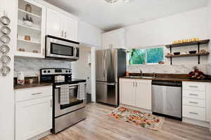 Kitchen featuring light hardwood / wood-style floors, white cabinets, stainless steel appliances, and backsplash