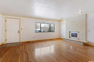 Unfurnished living room featuring ornamental molding, hardwood / wood-style floors, a brick fireplace, and a textured ceiling