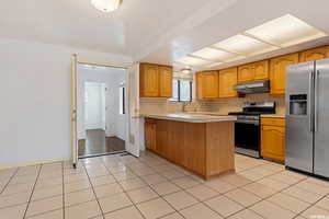 Kitchen with kitchen peninsula, light tile patterned floors, stainless steel fridge with ice dispenser, gas range oven, and sink