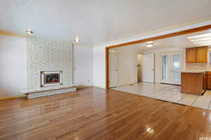 Unfurnished living room with light hardwood / wood-style floors, a textured ceiling, and a brick fireplace