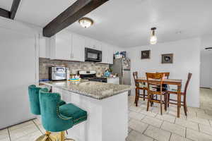 Kitchen with decorative backsplash, beam ceiling, appliances with stainless steel finishes, white cabinetry, and light stone countertops