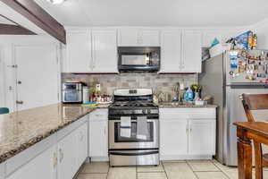 Kitchen with sink, white cabinetry, stainless steel appliances, light stone counters, and light tile patterned floors