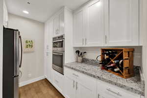 Kitchen with white cabinetry, light stone counters, stainless steel appliances, and light wood-type flooring