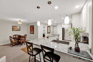 Kitchen/dining featuring light colored carpet, decorative light fixtures, light granite counters, and stainless steel refrigerator