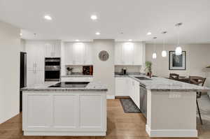 Kitchen featuring light granite countertops, light hardwood / wood-style floors, stainless steel appliances, pendant lighting, and white cabinets