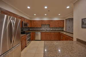 Kitchen with sink, tasteful backsplash, dark stone countertops, light tile patterned flooring, and appliances with stainless steel finishes for resident enjoyment.