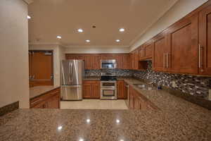 Kitchen with sink, tasteful backsplash, dark stone countertops, light tile patterned flooring, and appliances with stainless steel finishes for resident enjoyment.